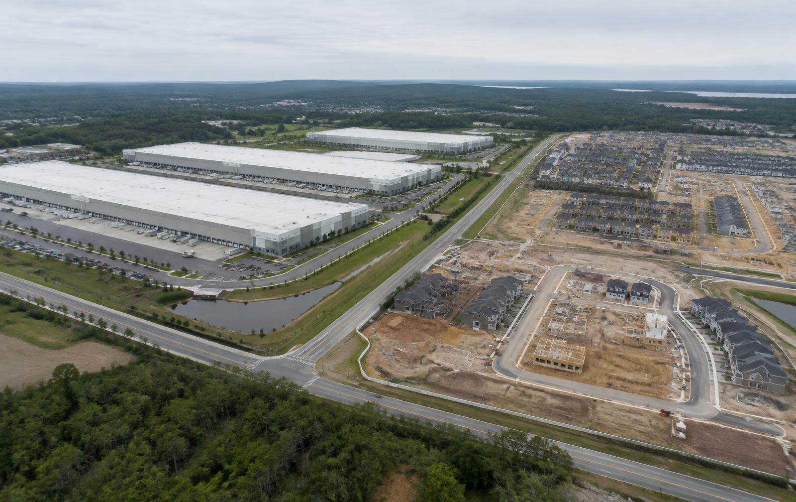 Aerial view of an industrial logistics campus beside a large residential community under construction